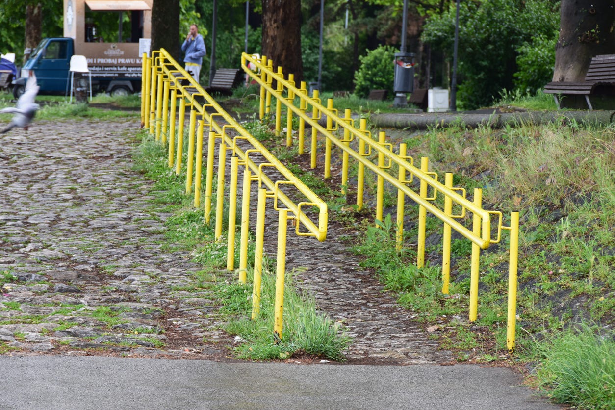 Steep way with cobble stones and grass but two handrails, one for wheelchair users