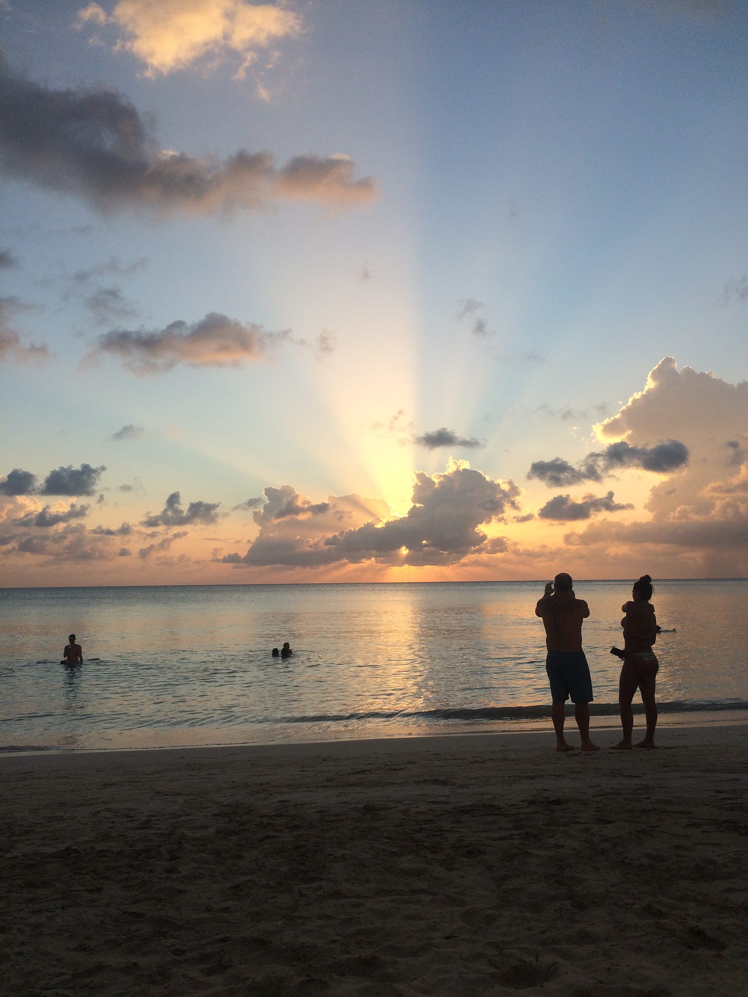 Couple standing on beach taking picture of sunset.