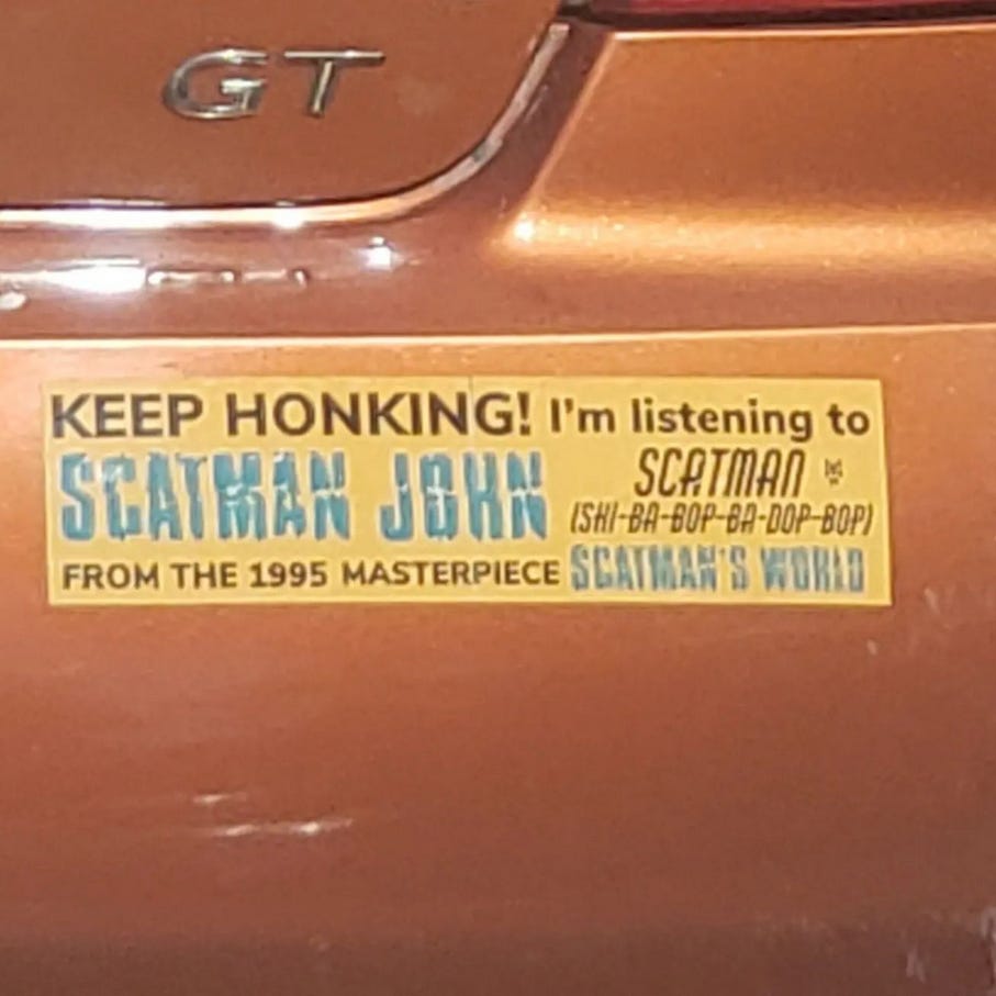 a bumper sticker on a car that says "Keep Honking! I'm listening to Scatman John Scatman (shi-ba-bop-ba-dop-bop) from the 1995 masterpiece Scatman's World"