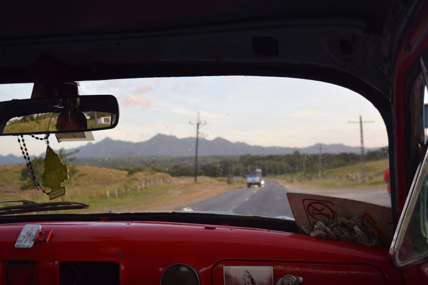 View out the front windshield of a car driving on a highway toward distant mountains at sunset