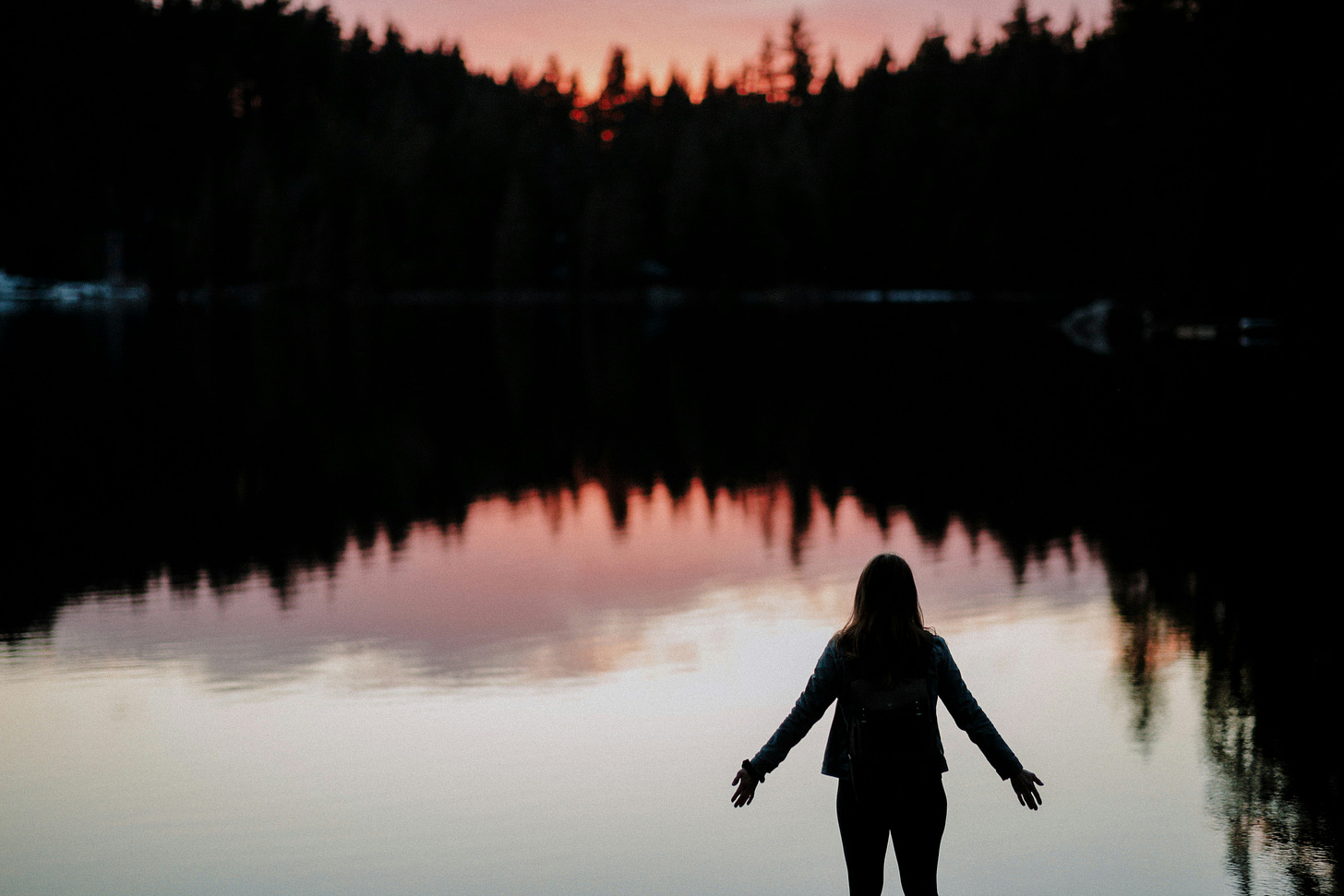 Image of woman with arms slightly extended overlooking a lake at dawn or dusk.