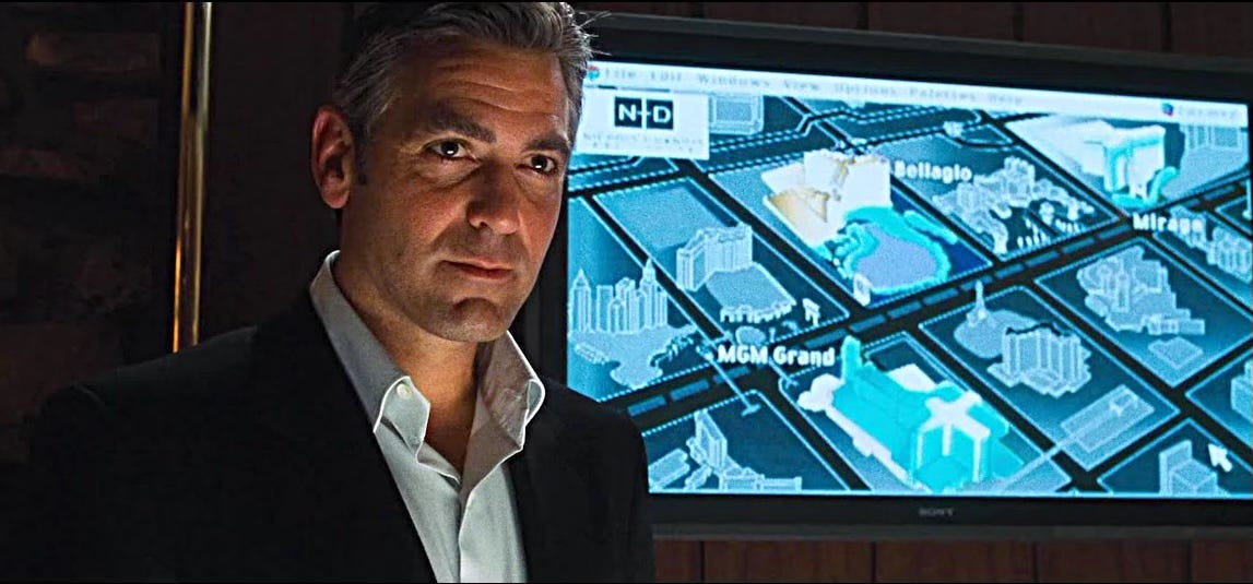 Ocean's 11 George Clooney looks to camera in front of a monitor showing a computer drawn map of the Las Vegas Strip.