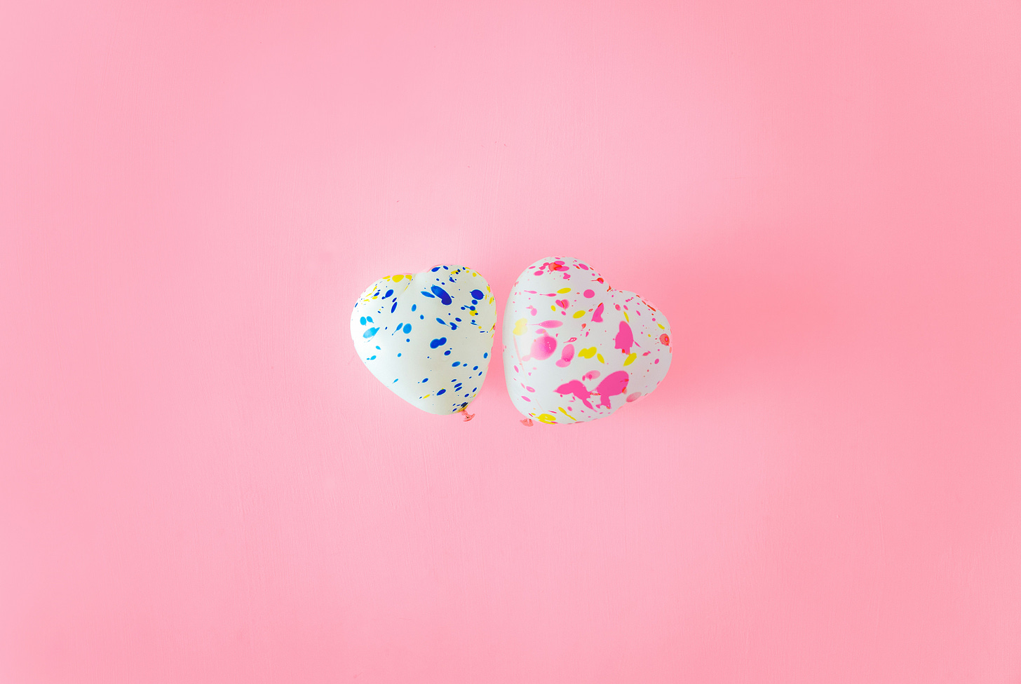 Two heart shaped balloons on a pink background