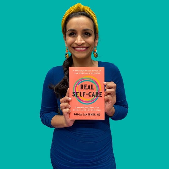 A woman wearing a blue shirt and yellow headband smiles and looks to the camera as she holds a book, Real Self-Care, against a teal background.