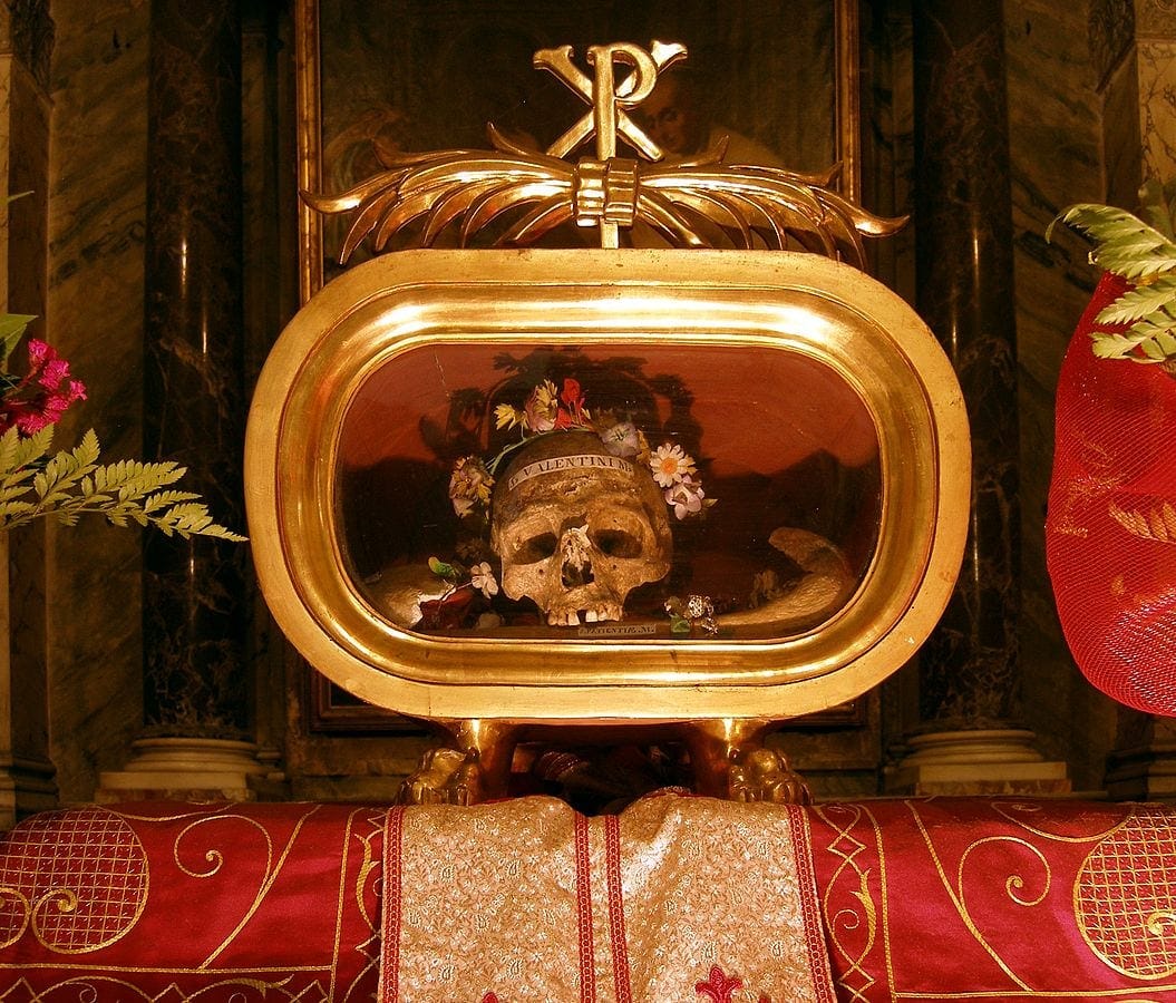 Skull with a flower crown on display in a church surrounded by gilded objects and red panels with hearts Skull with a flower crown on display in a church surrounded by gilded objects and red panels with hearts