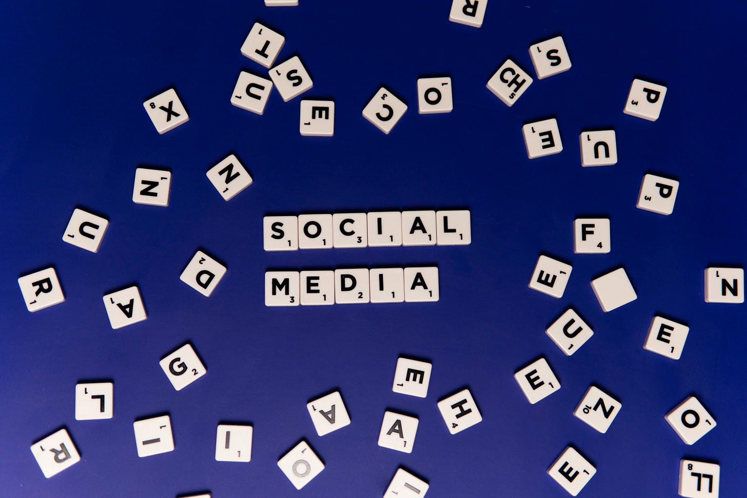 Scrabble game blocks with "Social Media" spelled out in the center of a pile of miscellaneous letters.