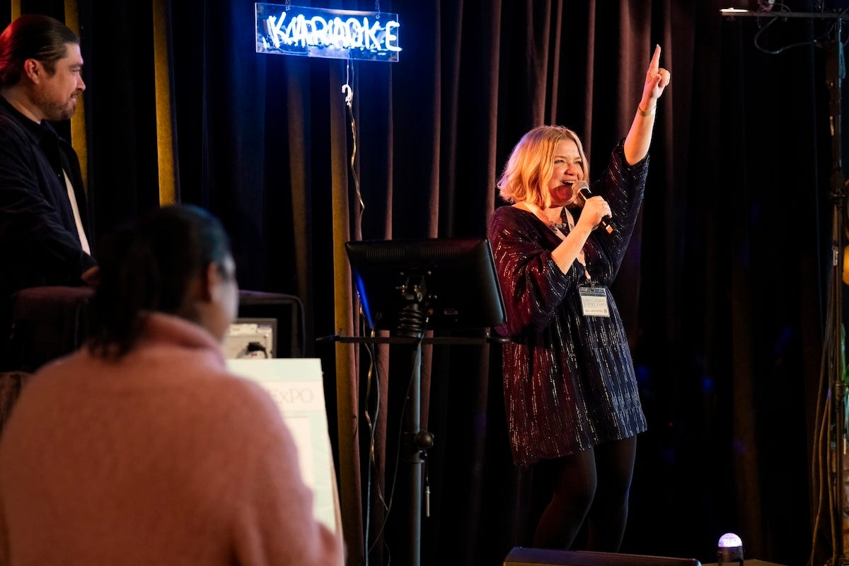 Mary Catherine Garrison performs karaoke on the set of Somebody Somewhere in front of brown velvet curtains