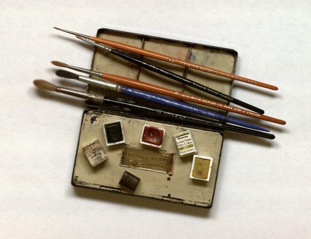 Photograph of a watercolor box with brushes and dry cakes of paint