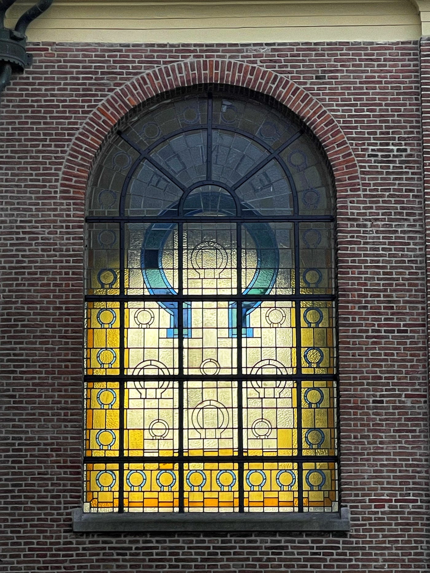 A stained glass church window in bright blue and yellow colors. Unlike the French cathedral type, this one has Art Deco elements. It’s a 1924 design, being replicated in the 1990s.