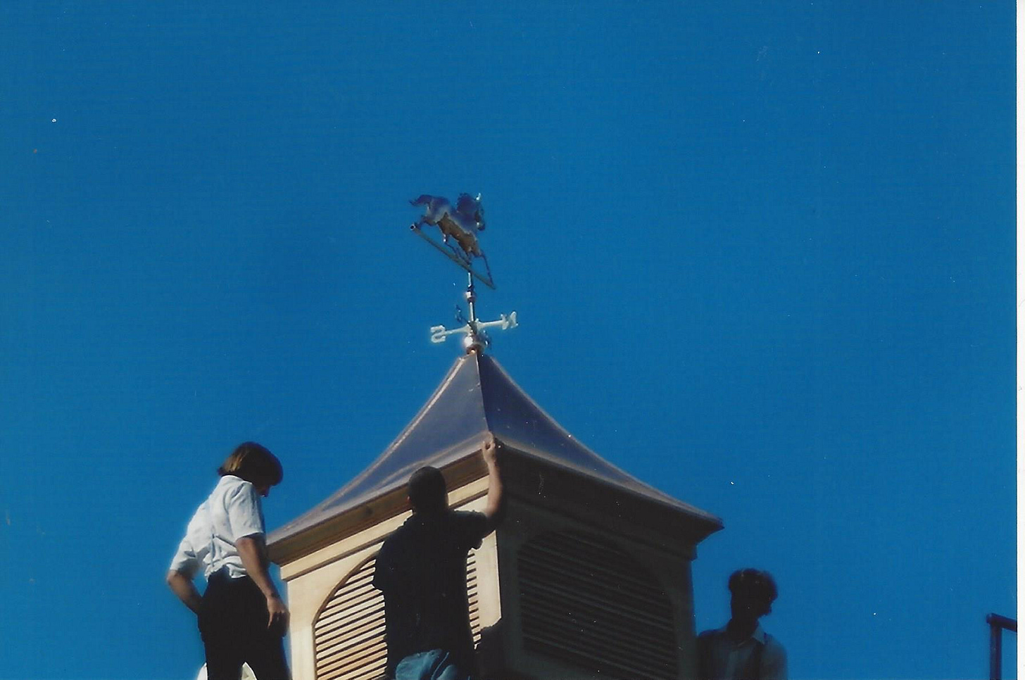 Workers place a cupola with a copper weather vane atop a barn