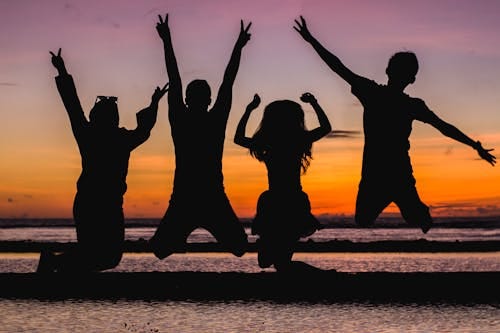 Free Silhouette of friends jumping on the beach at sunset, celebrating summer fun. Stock Photo