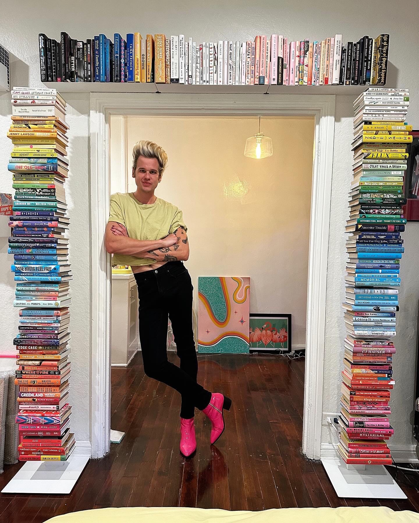 A photo of author Greg Mania standing in a doorway framed by his color-coded book collection