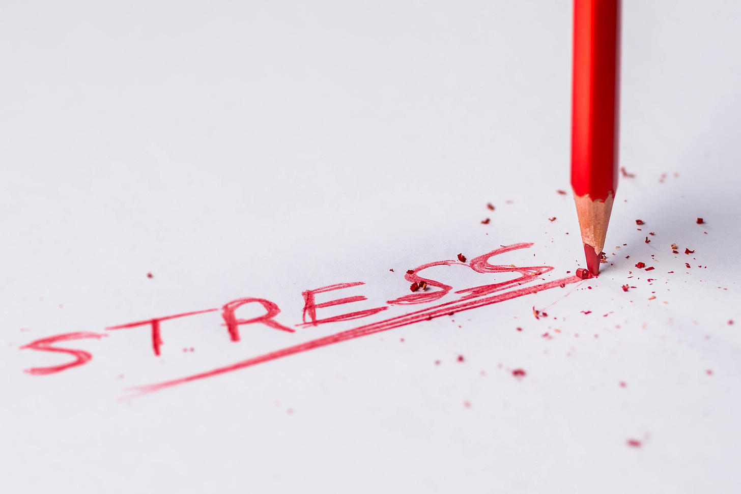 The word “stress” is written in red pencil on a white paper. The pencil is being pressed down hard.