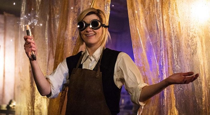 This image shows the Thirteenth Doctor (played by Jodie Whittaker) wearing a pair of goggles and the Twelfth Doctor's clothes. She smiles while holding her newly built sonic screwdriver in her right hand. This image shows the Thirteenth Doctor (played by Jodie Whittaker) wearing a pair of goggles and the Twelfth Doctor's clothes. She smiles while holding her newly built sonic screwdriver in her right hand.