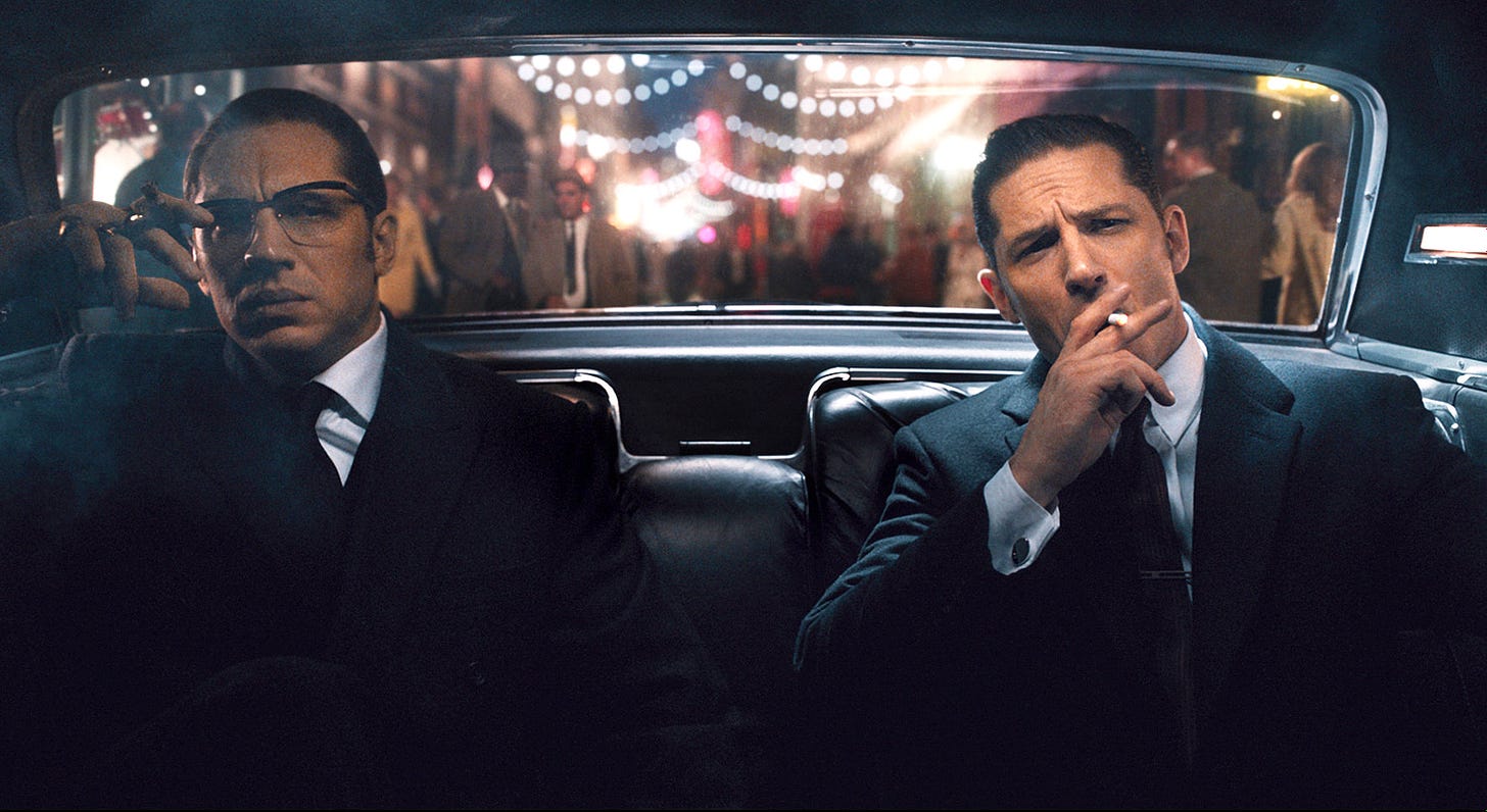 Movie still from Legend. Twin men sit in a car, well-dressed and one smoking a cigarette