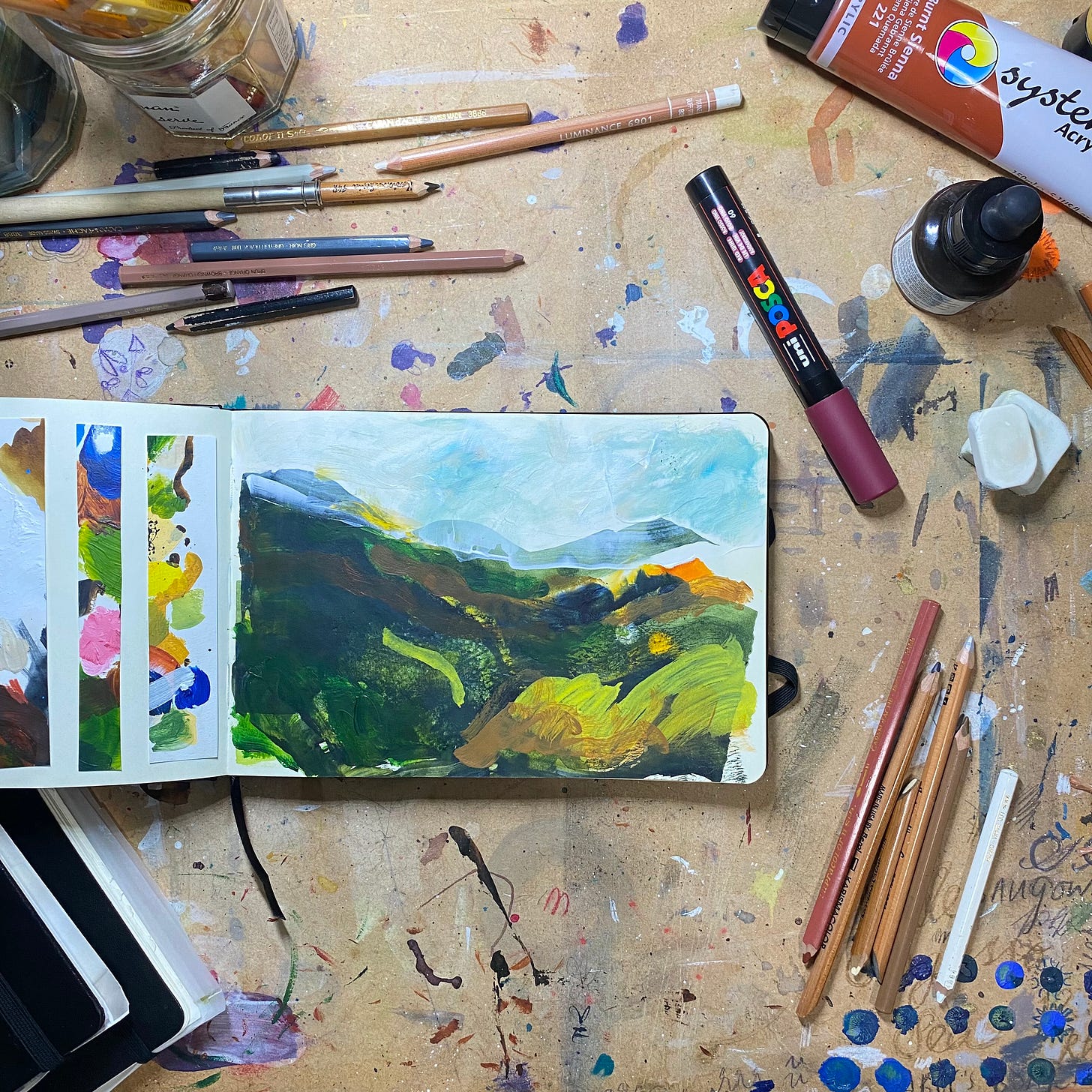 A landscape sketchbook with an illustration of rolling hills surrounded by art materials