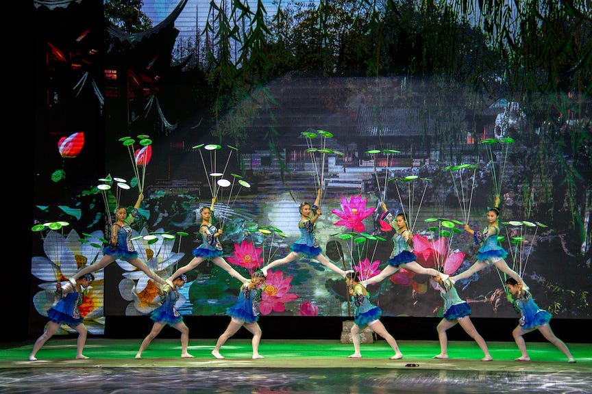 picture with 6 women on stage, 5 women standing on their shoulders. All of them are spinning multiple platers