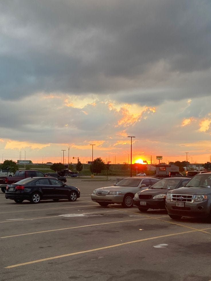 This may contain: a parking lot filled with lots of parked cars under a cloudy sky at sunset or sunrise