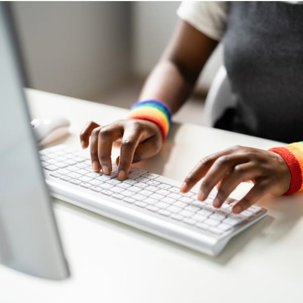 Two hands wearing rainbow sweatbands, types at a white keyboard.