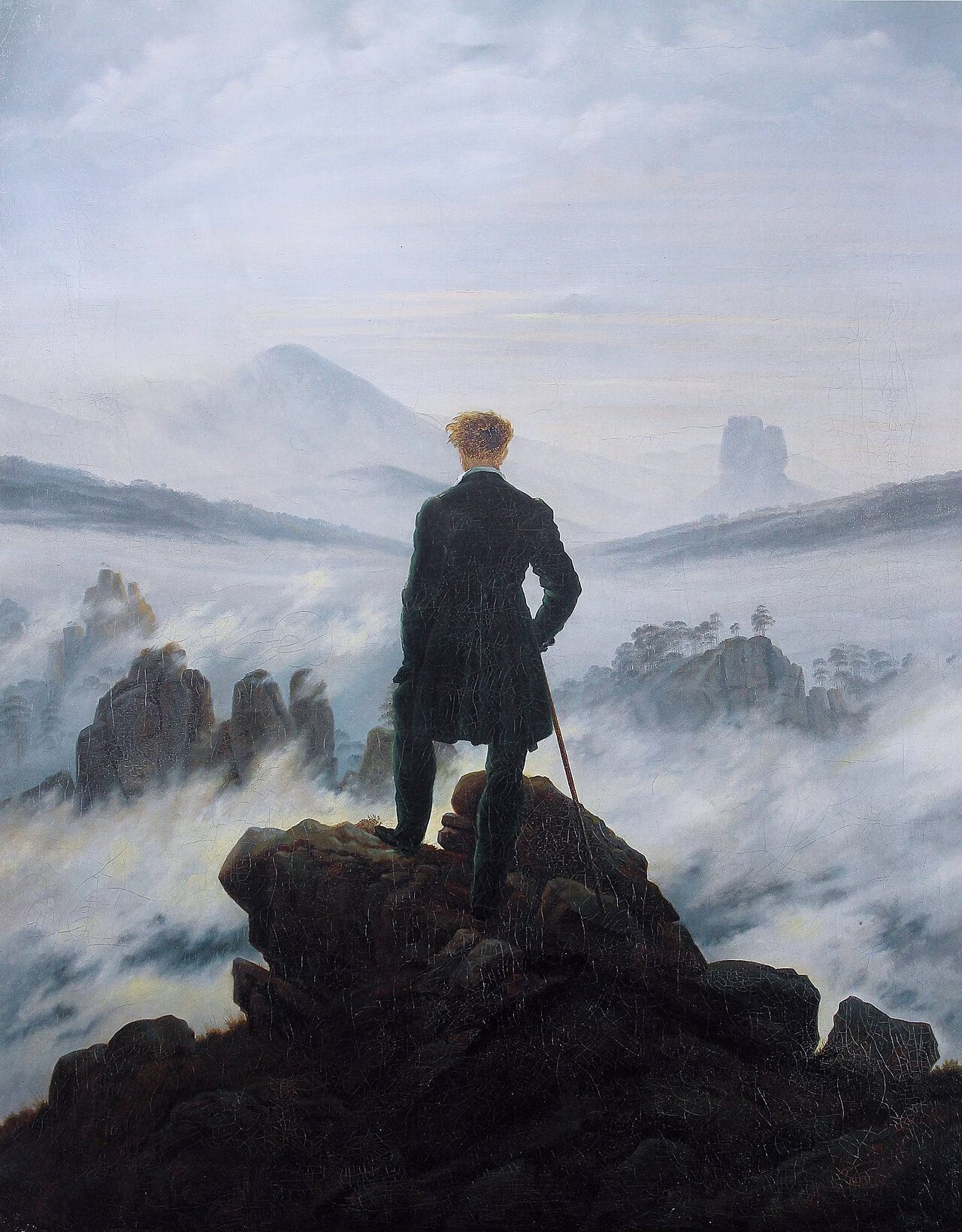 A man standing on a mountain looking out into the vast lands and fog below him