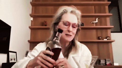 Meryl Streep wearing tinted rose-colored glasses pausing to think before chugging out of a bottle of red wine