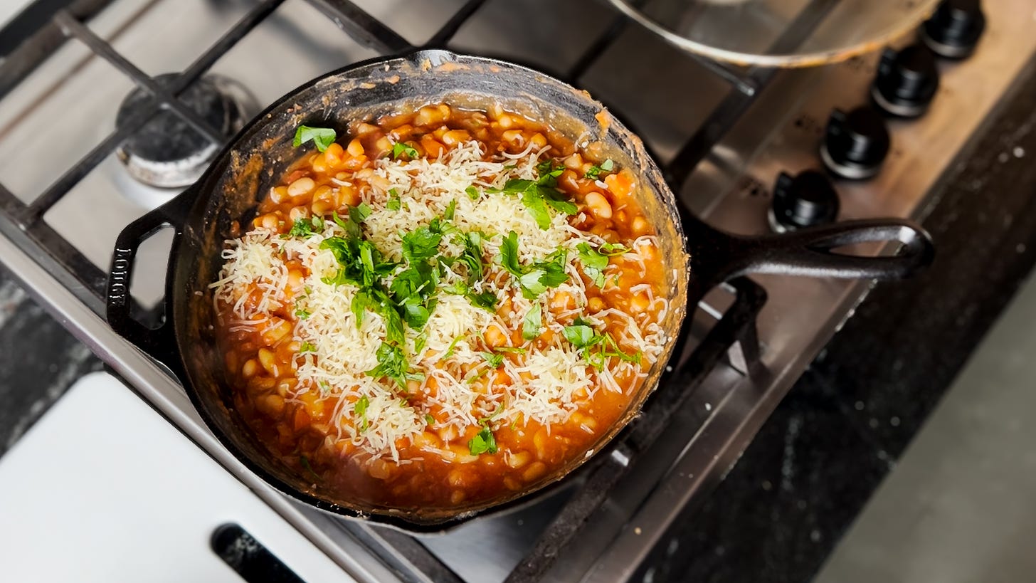 A cast iron skillet filled with bean stew topped with melted cheese and parsley