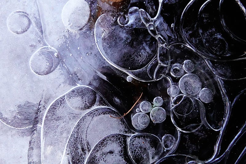 Fluid contour lines and air bubbles decorate the ice covering the water