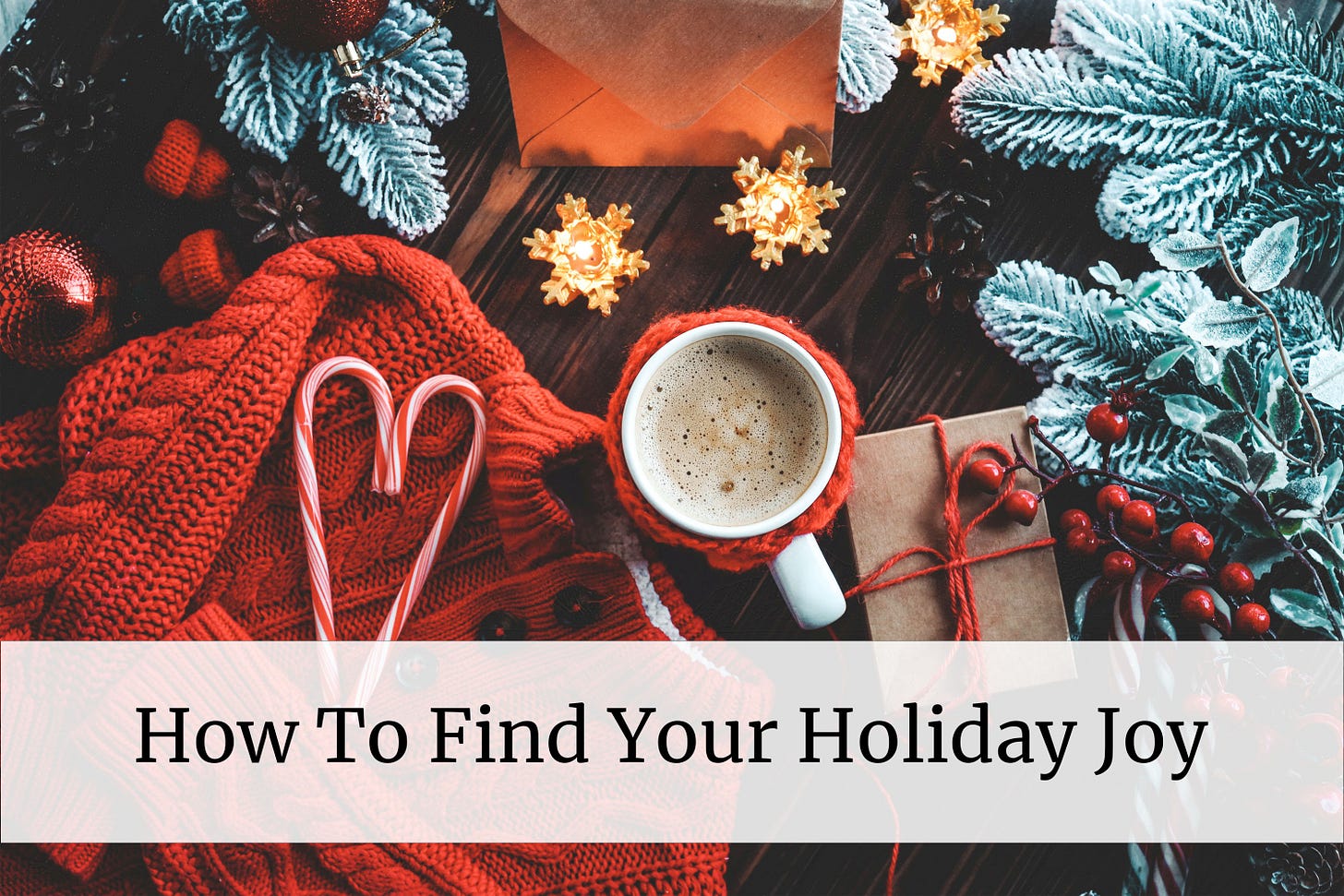 A wooden table with a red cup of coffee and a red sweater, two candy canes forming a heart, star-shaped candles, a small gift wrapped in brown paper and tied with red twine. Around the borders there are some snow-tipped pine branches. Overlay text reads “How To Find Your Holiday Joy”