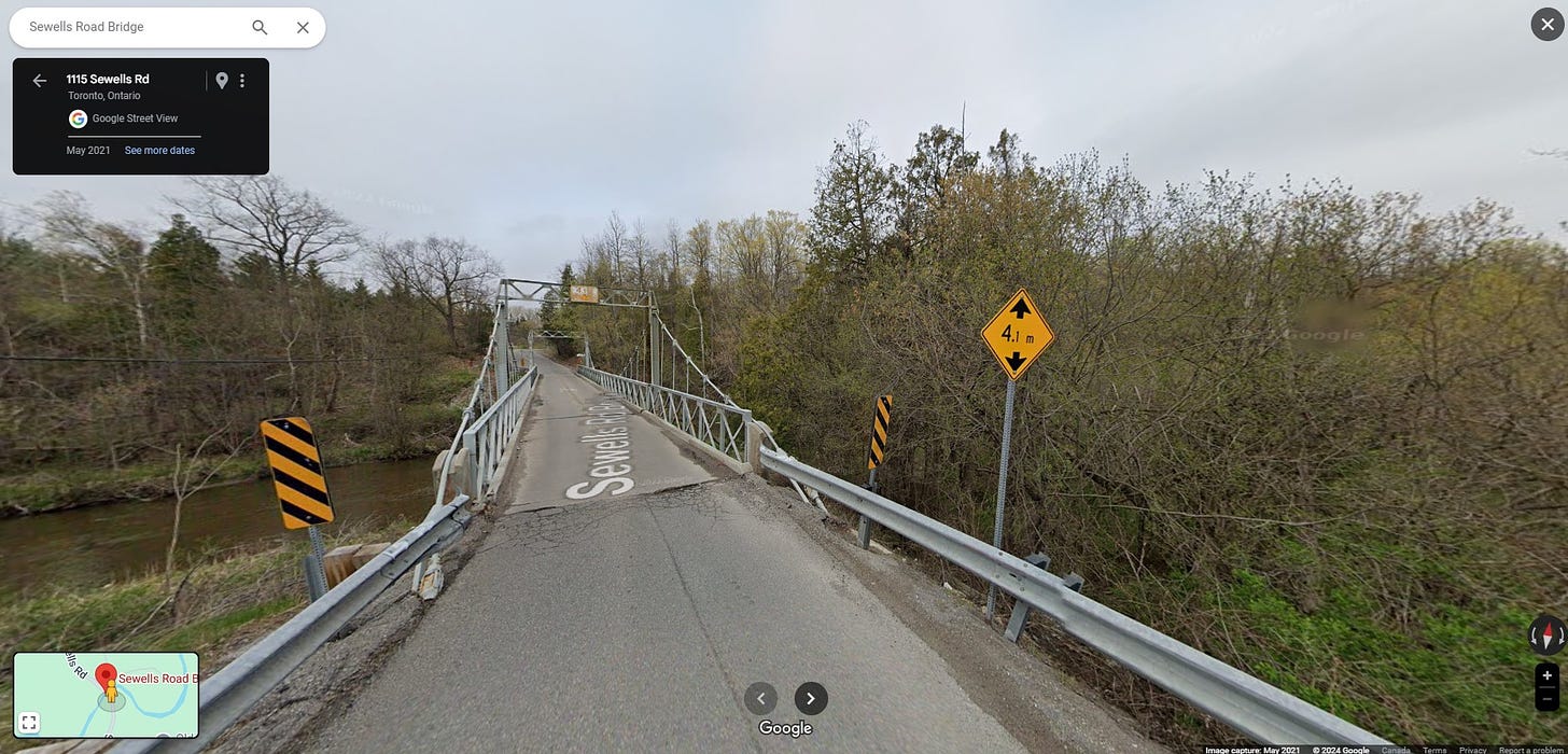 A Street View screengrab of the Sellers Road Suspension Bridge. Like in the previous photo, it is May 2023 and the surroundings are starting to green up, but are still quite drab. 