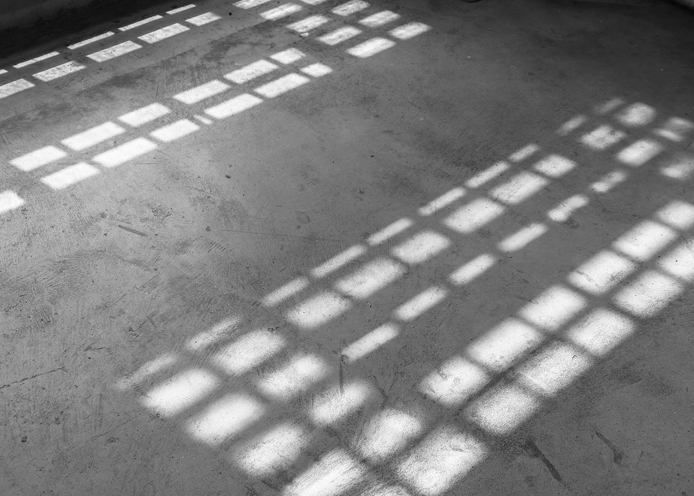 Shadows cast by a barred window across a cell floor, black and white image