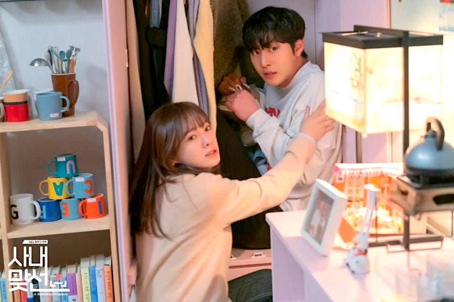 Two hot Korean actors: the woman is stuffing the man into a freestanding closet in a childhood bedroom