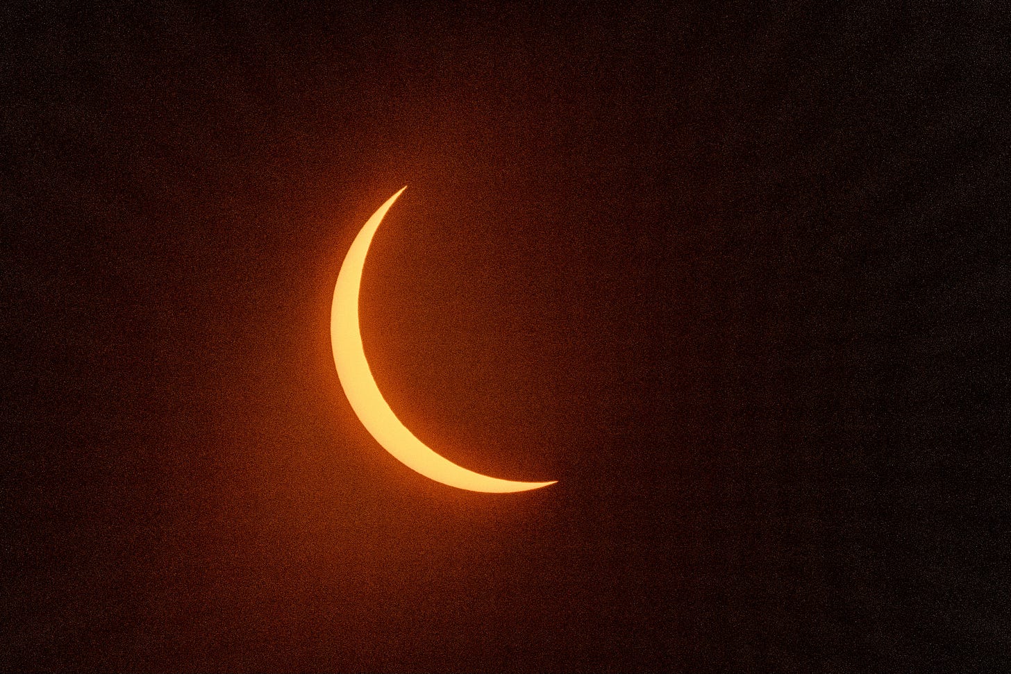 A slender orange crescent, slightly furred from lens glare, of the sun in partial solar eclipse
