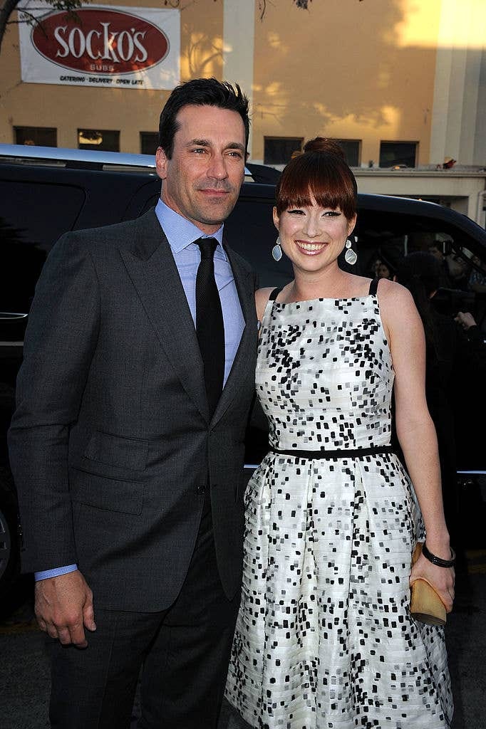Man in suit and woman in patterned dress with earrings posing on a sidewalk