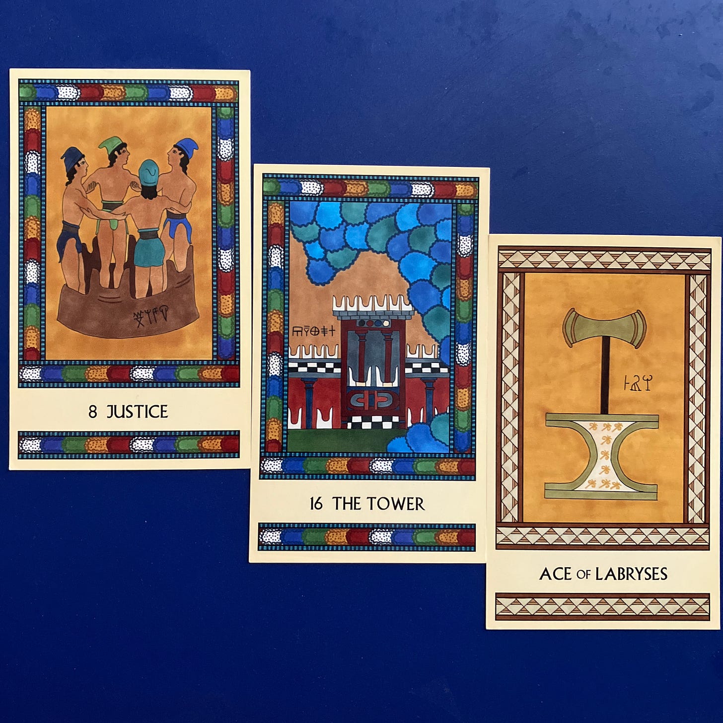 Three Minoan Tarot cards lying on a deep blue background. Justice shows four loincloth-clad people stomping grapes in a large vat, their arms interlinked so each person's movements affect the others. The Tower shows a Minoan temple being inundated by a tidal wave. The Ace of Labryses shows a large gold labrys standing upright atop an incurved altar.