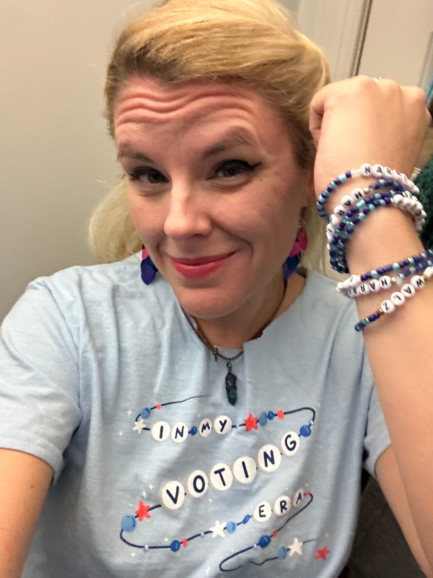 Cass smiling, showing off an armful of friendship bracelets, dressed in a blue "In my voting era" T-shirt