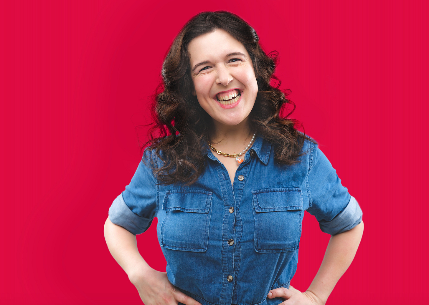 Woman in denim stands in front a red wall, smiling