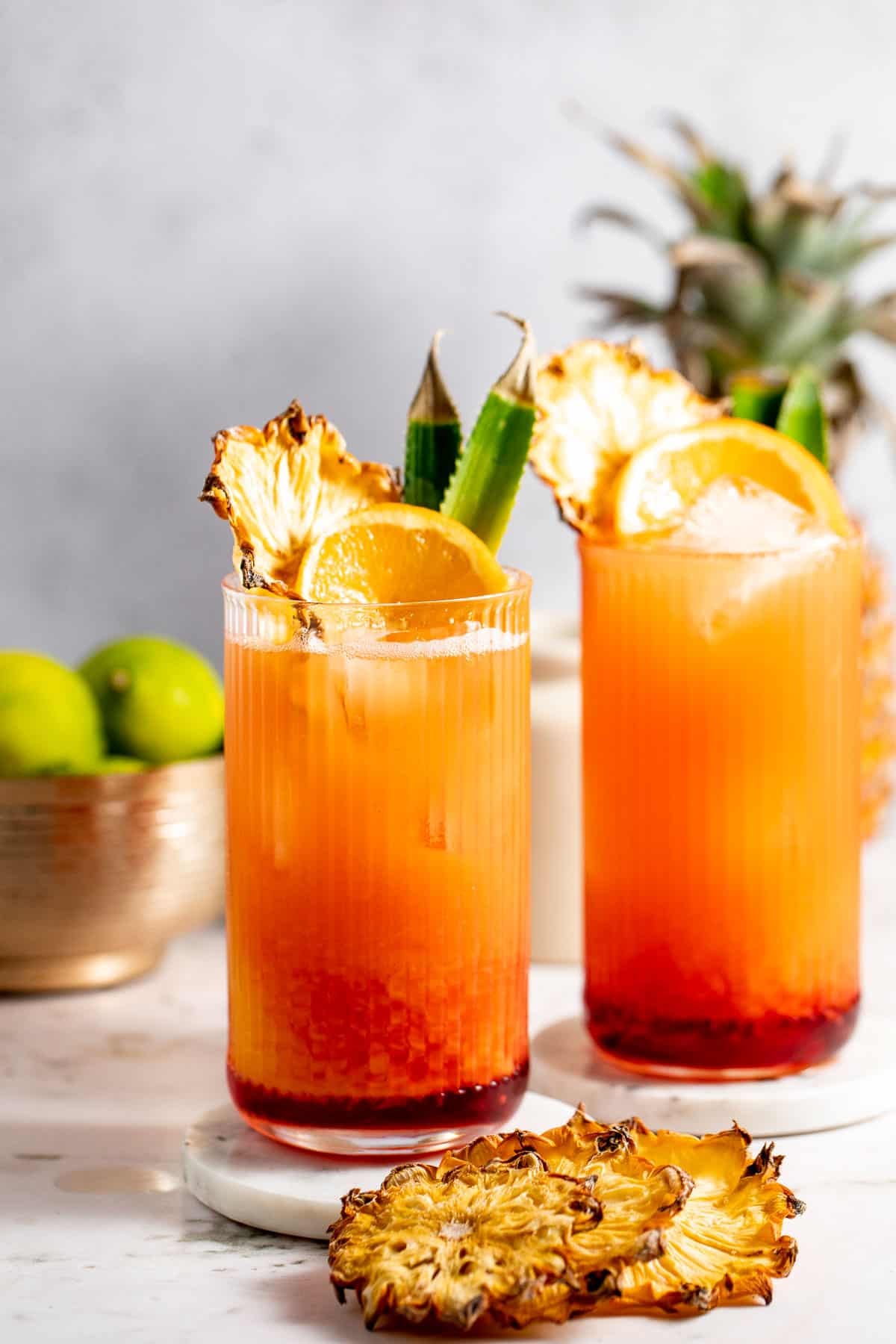 two highball glasses garnished with dehydrated pineapple on grey background