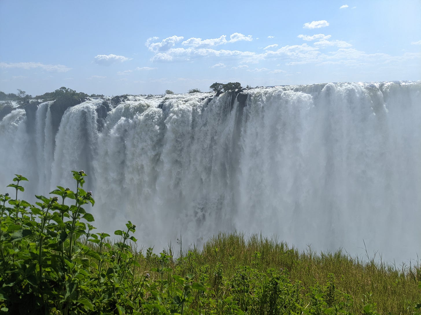 photo of a large waterfall against a blue sky with trees in the foreground