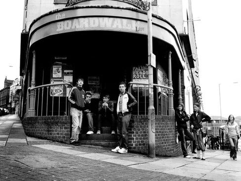The original Arctic Monkeys line-up outside the entrance to The Boardwalk in a black and white photo The original Arctic Monkeys line-up outside the entrance to The Boardwalk in a black and white photo