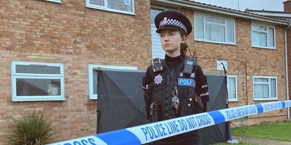 Female police officer scene guard with buildings behind and police-do not cross tape in front