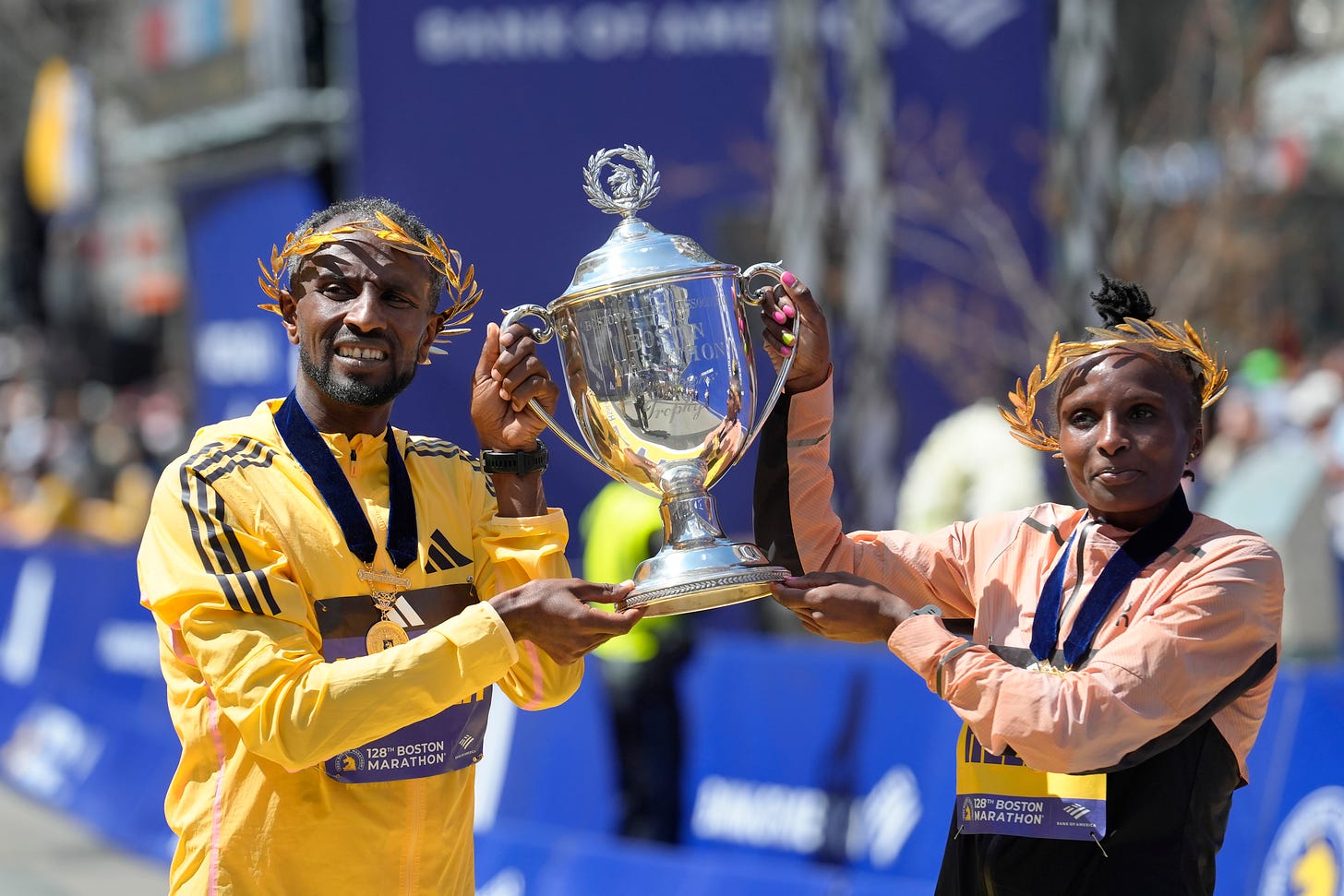 Sisay Lemma, of Ethiopia, left, winner of the men's division of the Boston Marathon, and Hellen Obiri, of Kenya, right, winner of the women's division of the race, hold the trophy on the finish line of the Boston Marathon.
