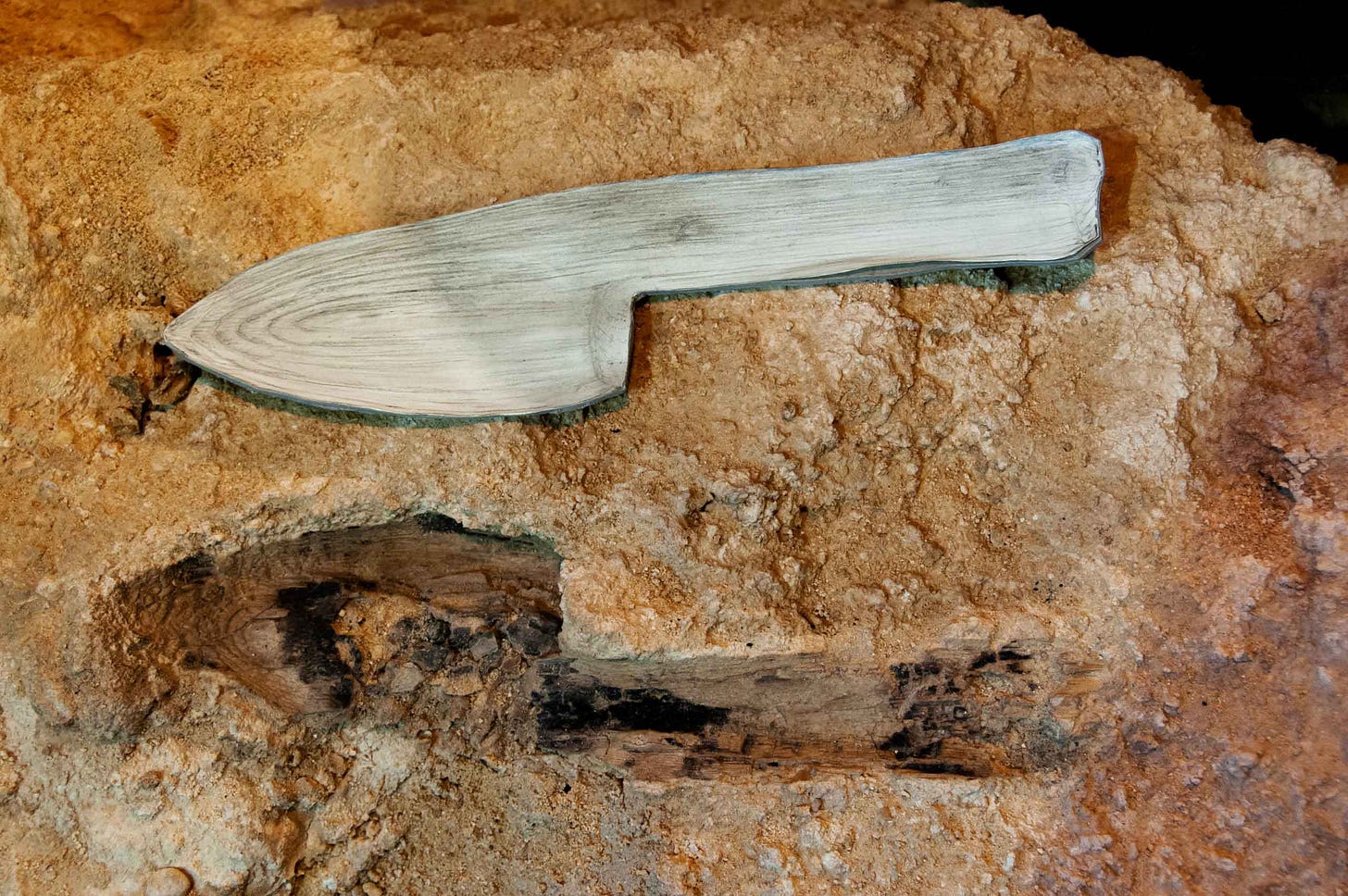 An imprint within an archaeological deposit in the shape of a knife or spade, with a wooden object of the same shape pictured above it An imprint within an archaeological deposit in the shape of a knife or spade, with a wooden object of the same shape pictured above it
