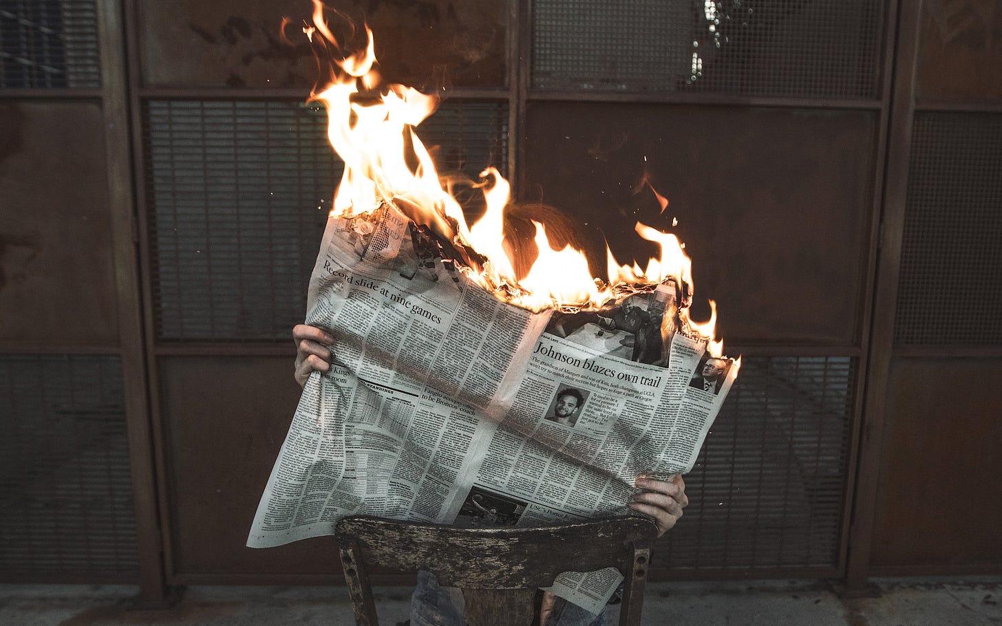 photo of a person holding and reading a newspaper that is on fire