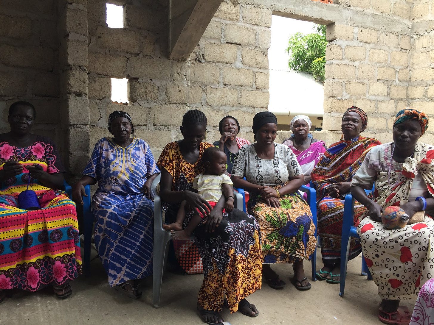 South Sudanese women in local dress, one holding a baby, sit in a group in a mud brick church.