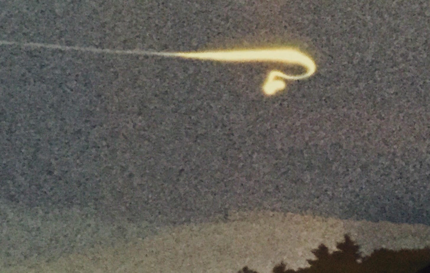 A photo of a oddly shaped light streak across the sky of a mountain range