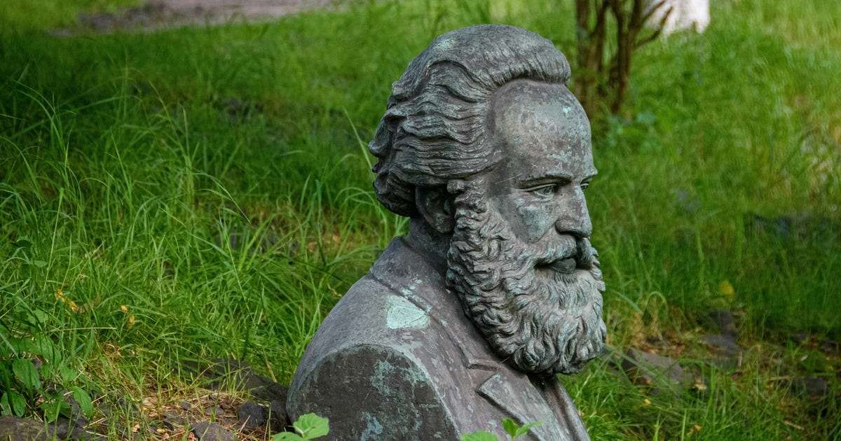 Photo from Unsplash, free to use. It shows a statue in profile, with a contemplative look and a beard, buried up to its shoulders in the grass.