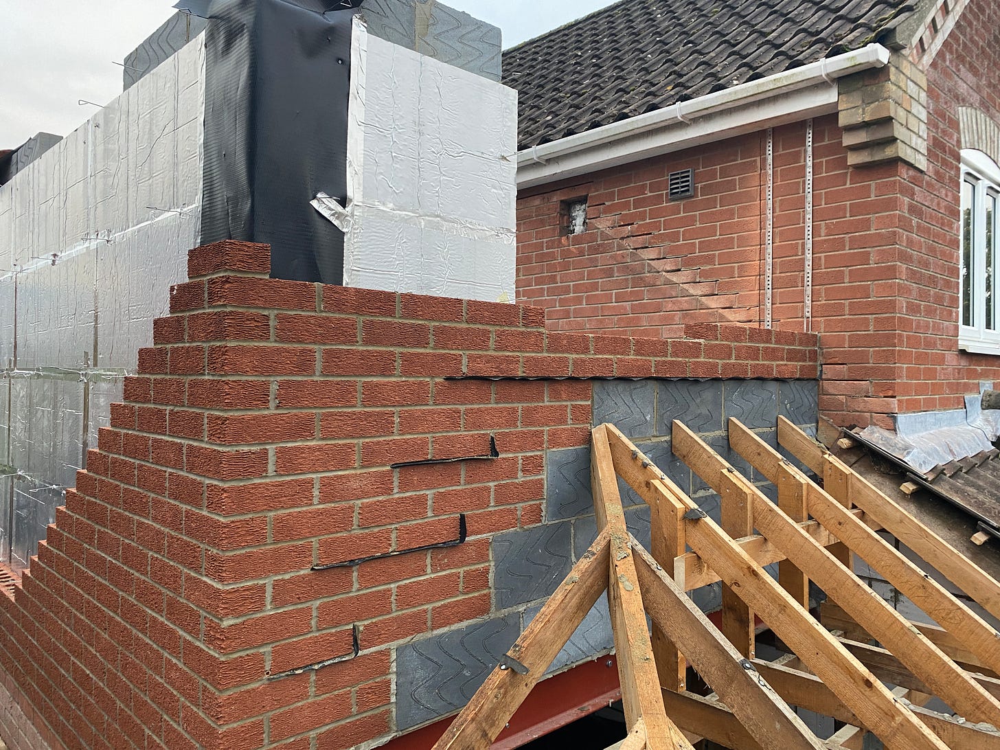 red bricks are being built up in front of the cavity wall sheets