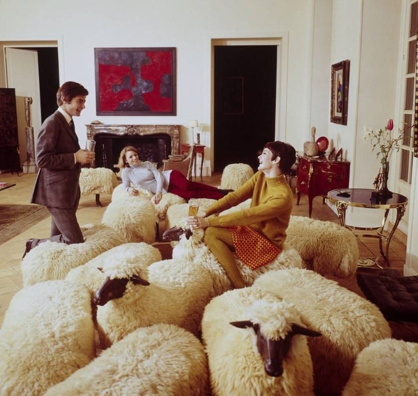 A flock of Lalanne sheep in a Paris apartment in the 1970s, with three people sitting on them having a conversation.