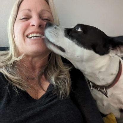 Jeanne laughing as black and white dog Moxie gives kisses