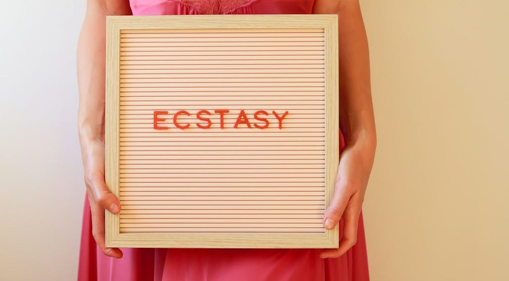 Woman holds a sign that reads "ecstasy."